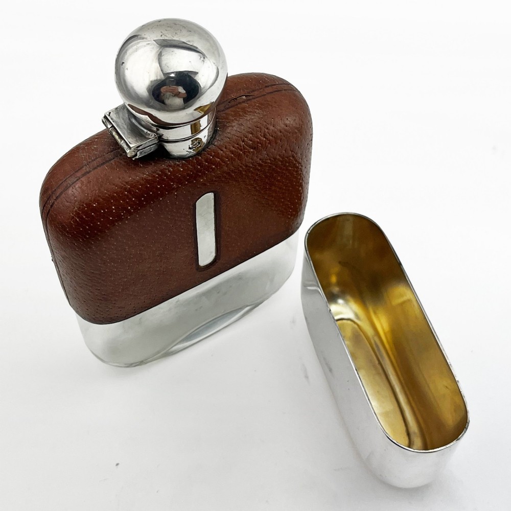 A silver plated hip flask featuring a textured brown leather upper section with a vertical sight window and a polished domed cap. View V