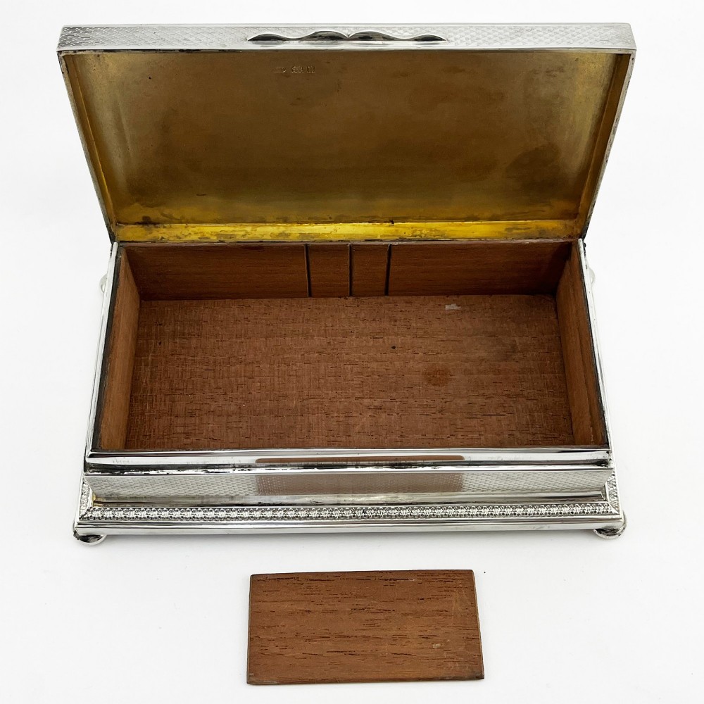 A rectangular sterling silver trinket box featuring engine-turned engraving, a beaded border, and a central engraved cartouche with initials. View VI