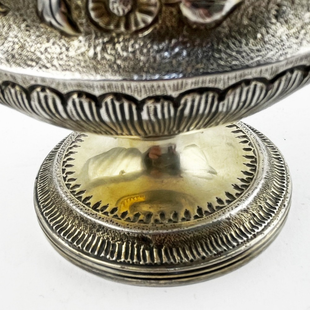 A George III sterling silver campana-shaped cup featuring chased floral motifs, a vacant cartouche, twin scroll handles, and a gilt interior. View V