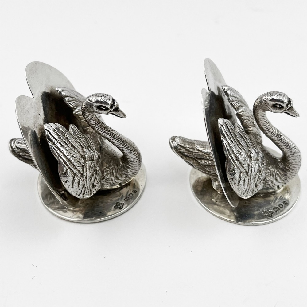 A pair of Edwardian sterling silver menu holders shaped as detailed swans resting on circular bases with central card slots.