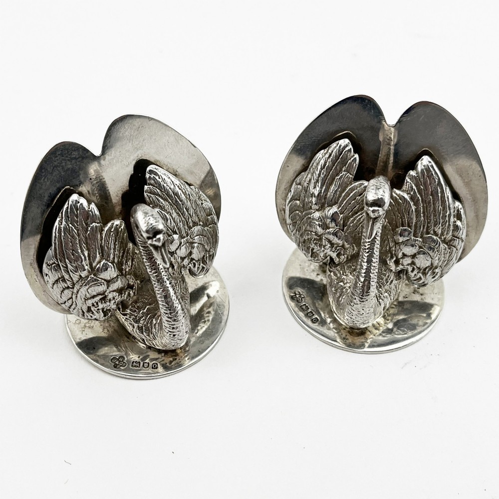A pair of Edwardian sterling silver menu holders shaped as detailed swans resting on circular bases with central card slots. View II