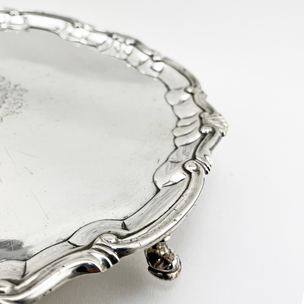 A circular George II sterling silver salver featuring a shaped shell-and-scroll border, cast feet, and a central engraved armorial crest. View II