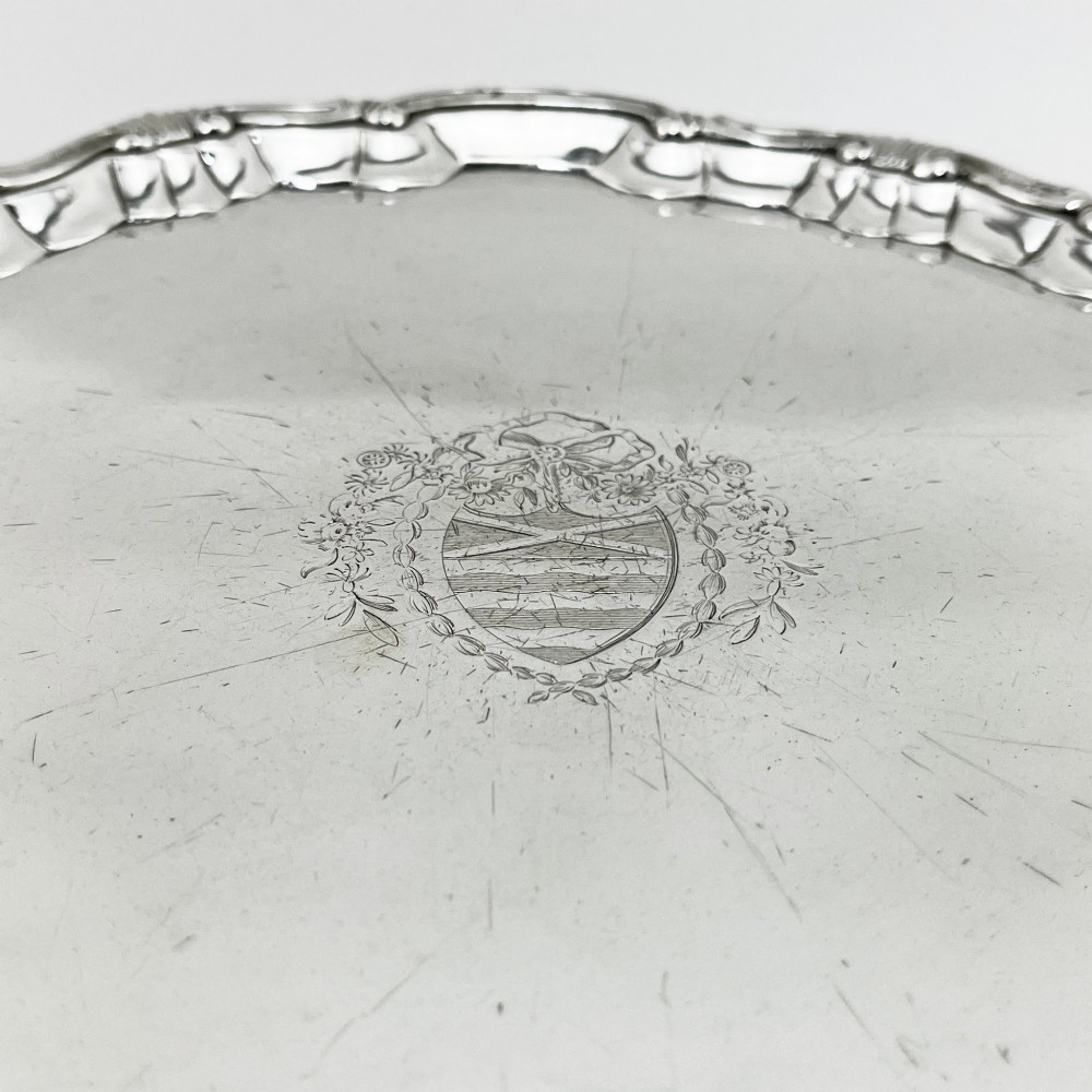 A circular George II sterling silver salver featuring a shaped shell-and-scroll border, cast feet, and a central engraved armorial crest. View VI