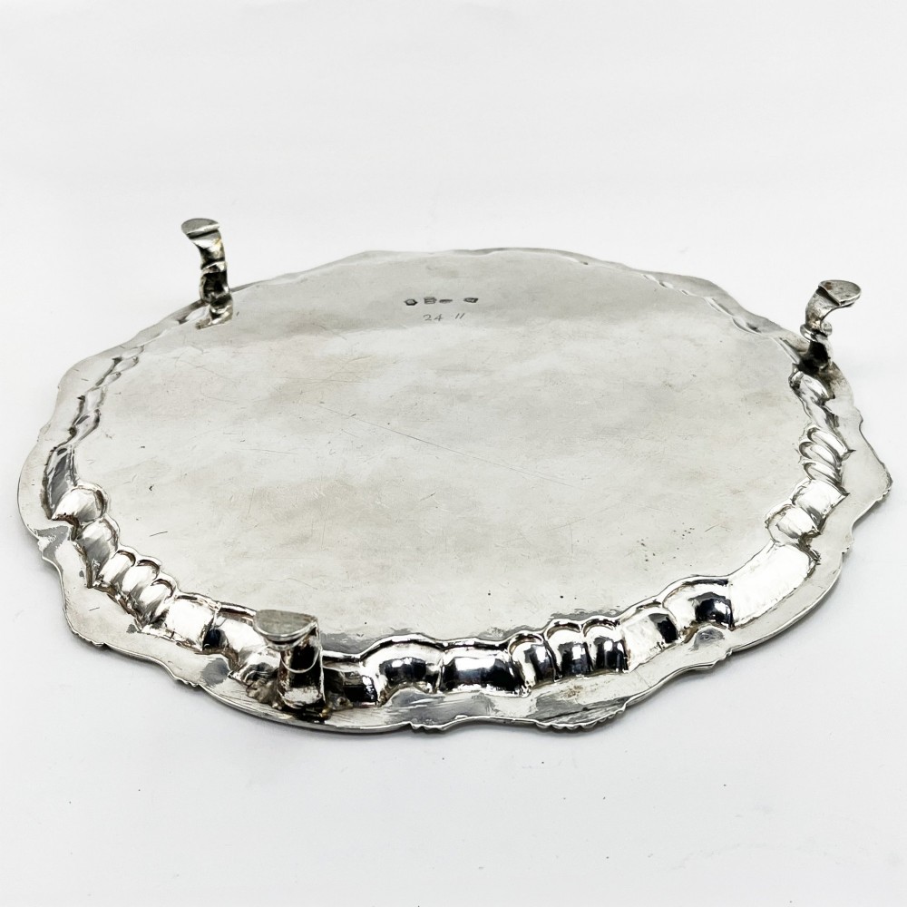 A circular George II sterling silver salver featuring a shaped shell-and-scroll border, cast feet, and a central engraved armorial crest. View VII