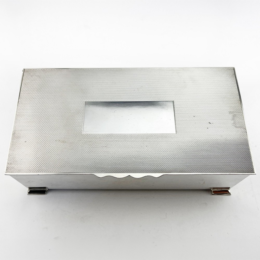 A rectangular sterling silver box featuring an engine-turned patterned lid, a central rectangular cartouche, and four stepped bracket feet. View IV