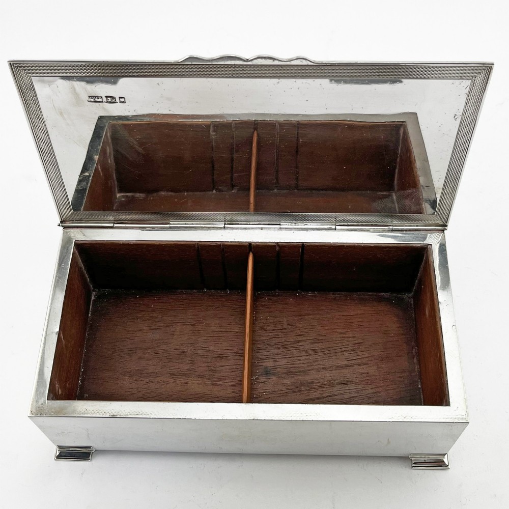 A rectangular sterling silver box featuring an engine-turned patterned lid, a central rectangular cartouche, and four stepped bracket feet. View VI