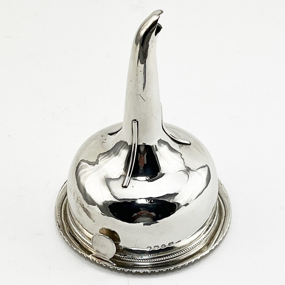 A Georgian sterling silver wine funnel resting on a beaded circular drip tray with visible hallmarks.