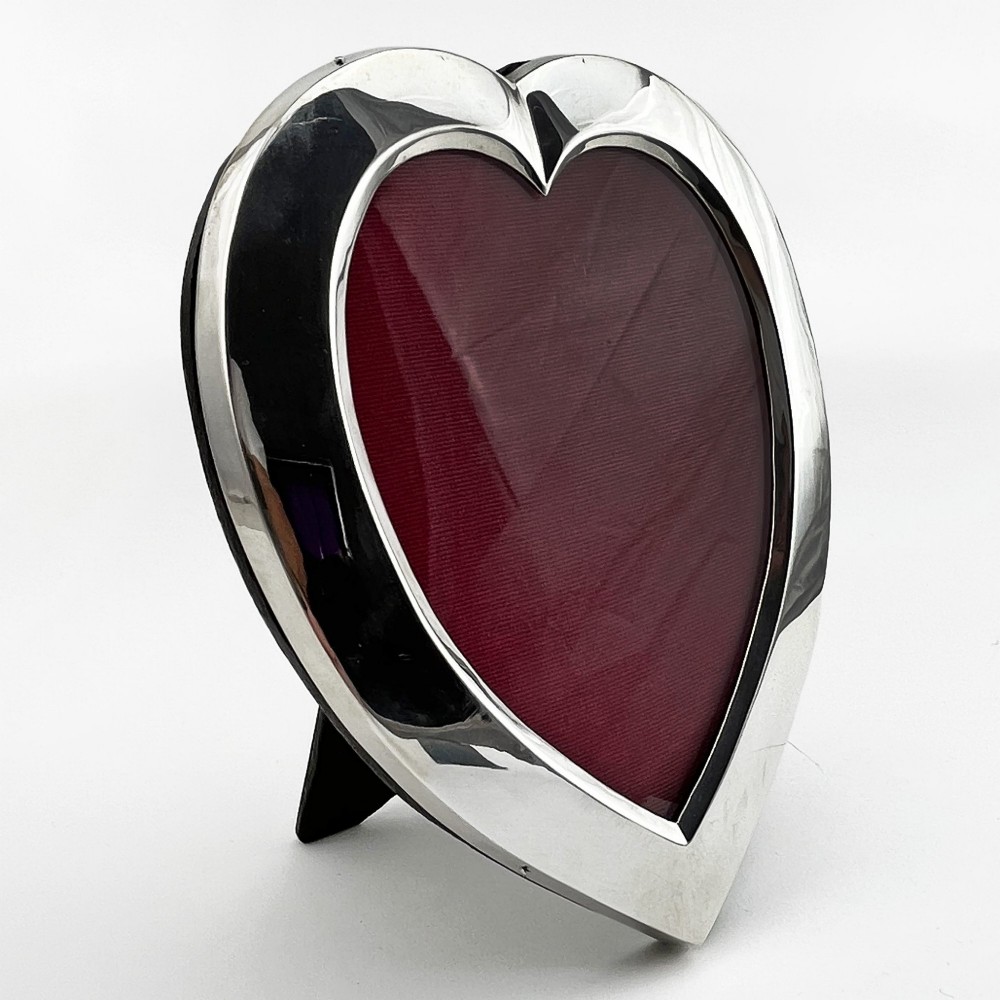 A heart-shaped sterling silver photo frame with a polished border, burgundy velvet backdrop, and an easel support leg.