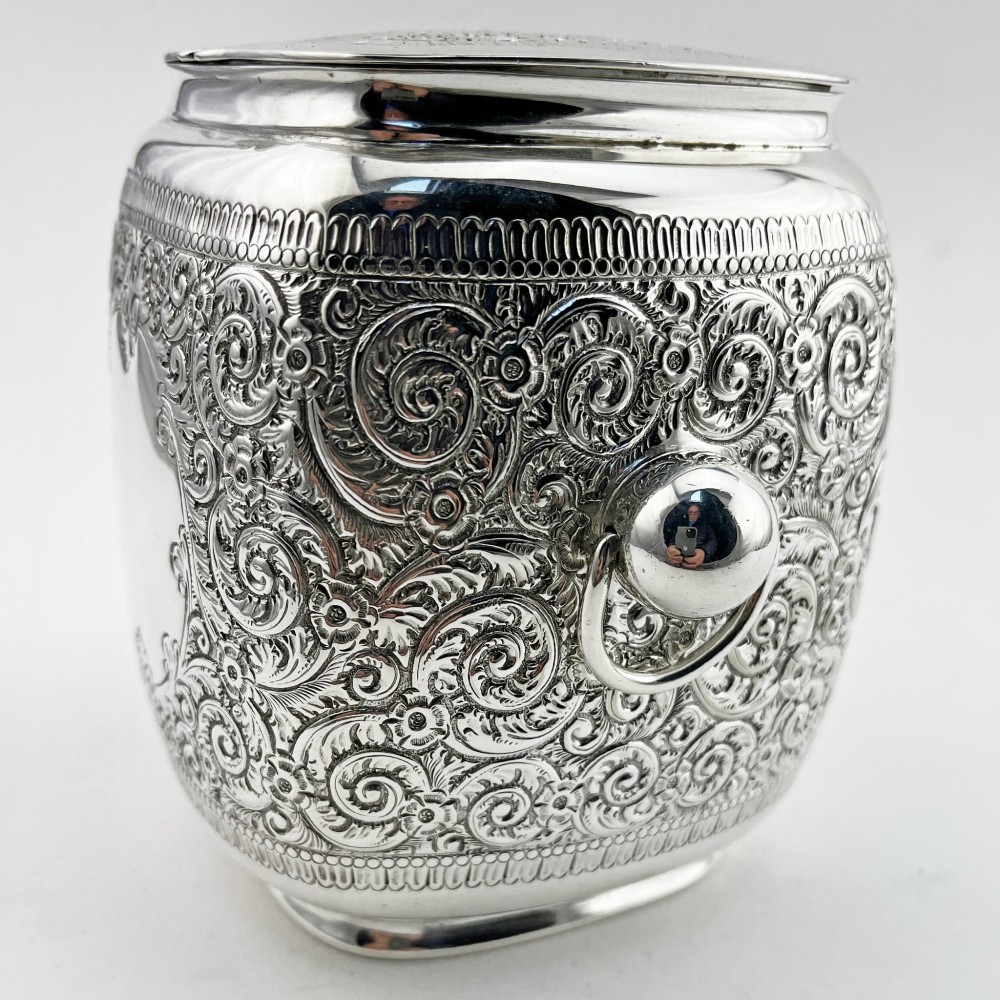A silver-plated rectangular tea caddy featuring elaborate floral engraving, side handles, and a central blank cartouche. View IV