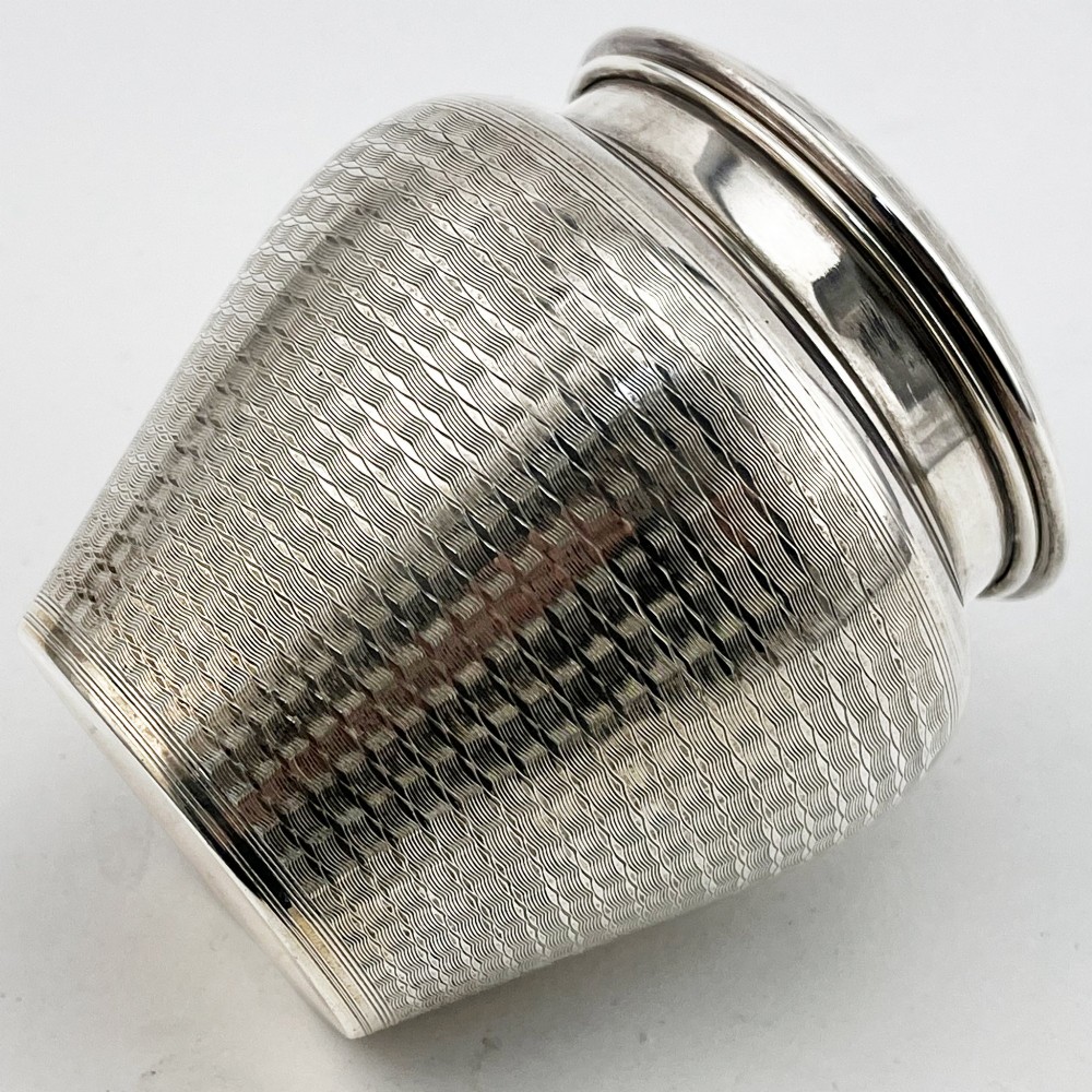 A rounded sterling silver tea caddy featuring a woven engine-turned textured pattern across the body and fitted circular lid, displaying British hallmarks. View IV