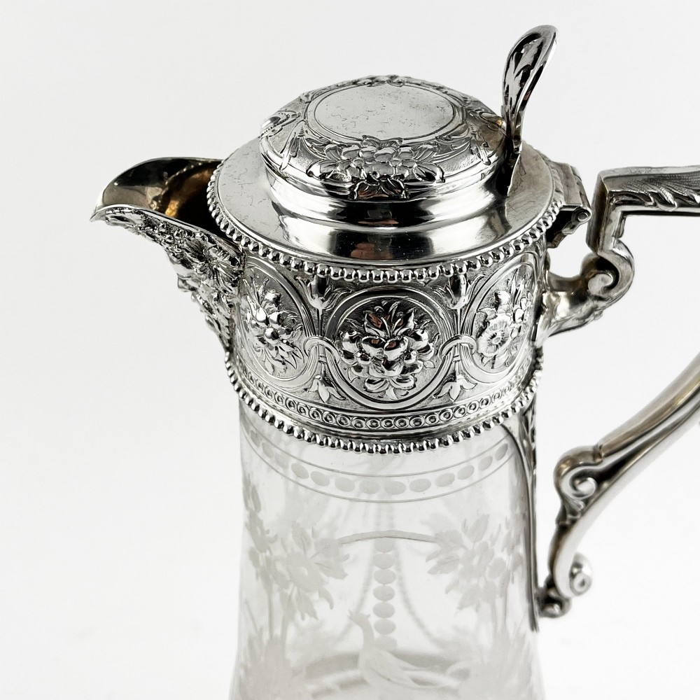 A Victorian sterling silver-mounted clear glass claret jug with floral glass etching, chased silver neck collar, and angular silver handle. View II