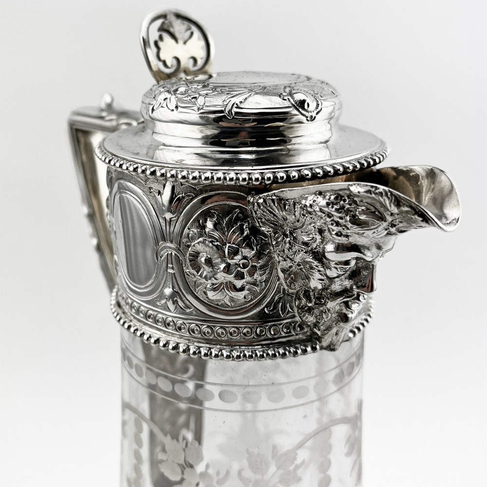 A Victorian sterling silver-mounted clear glass claret jug with floral glass etching, chased silver neck collar, and angular silver handle. View V