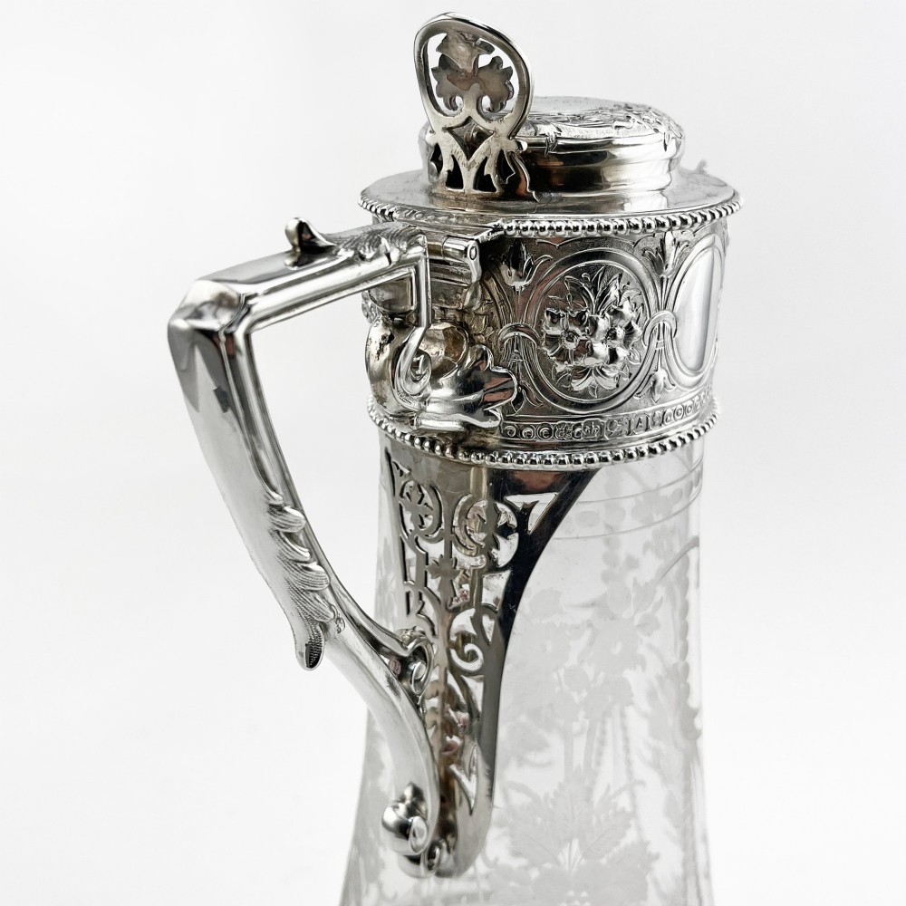 A Victorian sterling silver-mounted clear glass claret jug with floral glass etching, chased silver neck collar, and angular silver handle. View VI