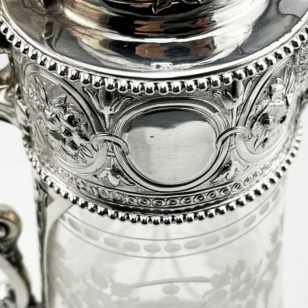 A Victorian sterling silver-mounted clear glass claret jug with floral glass etching, chased silver neck collar, and angular silver handle. View VII