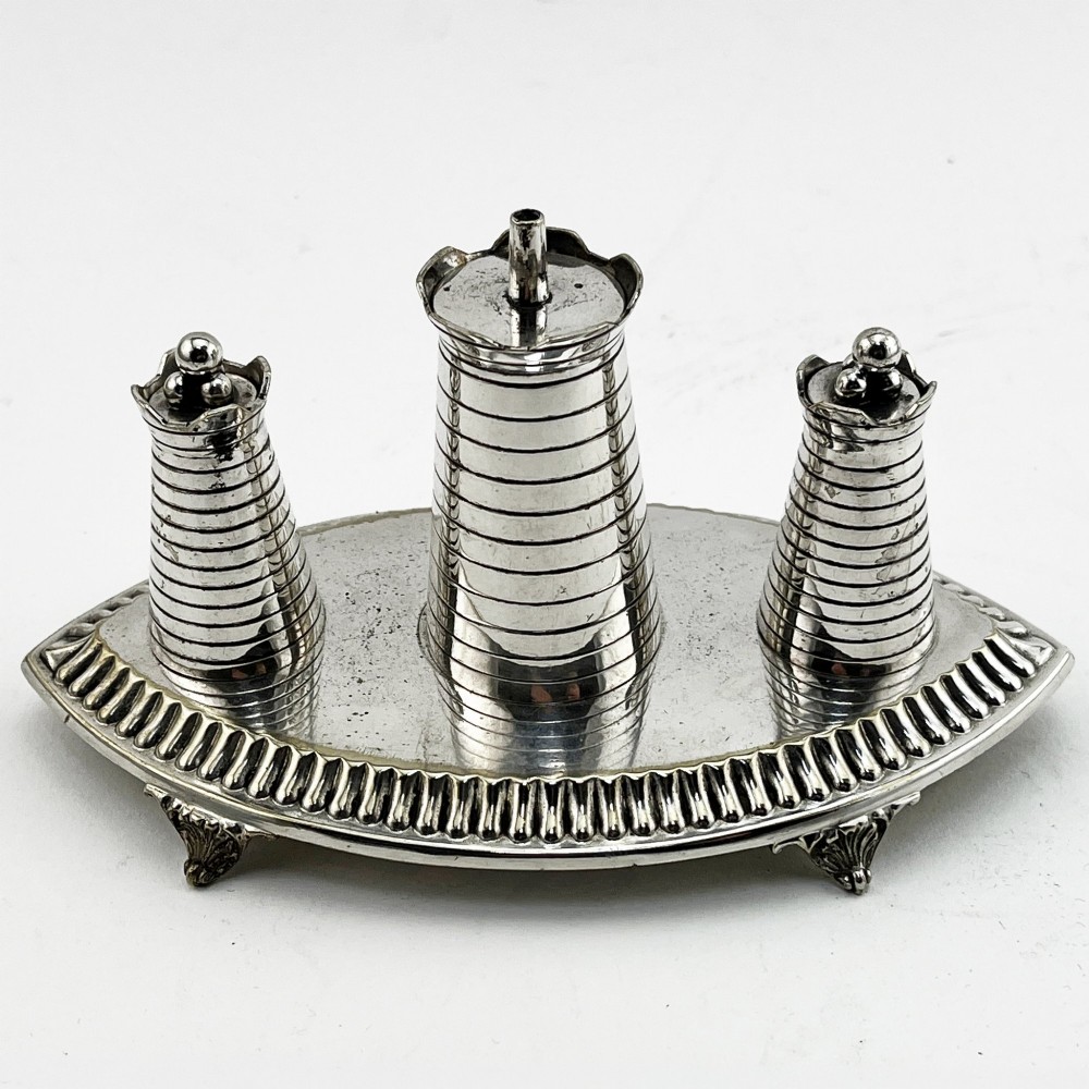 A silver-plated table cigar lighter featuring three horizontal-ribbed conical towers set on an oval tray with a gadrooned border and scrolled feet.
