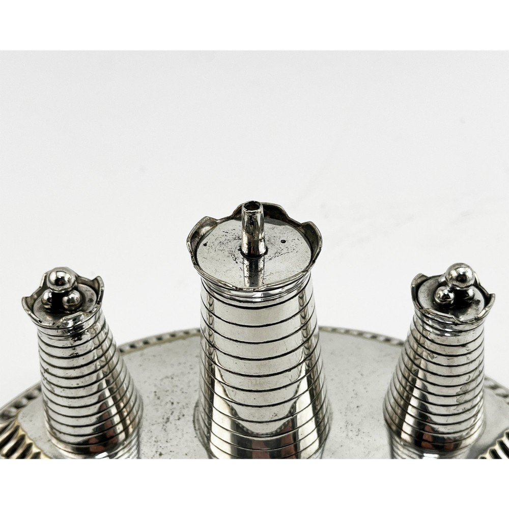 A silver-plated table cigar lighter featuring three horizontal-ribbed conical towers set on an oval tray with a gadrooned border and scrolled feet. View II