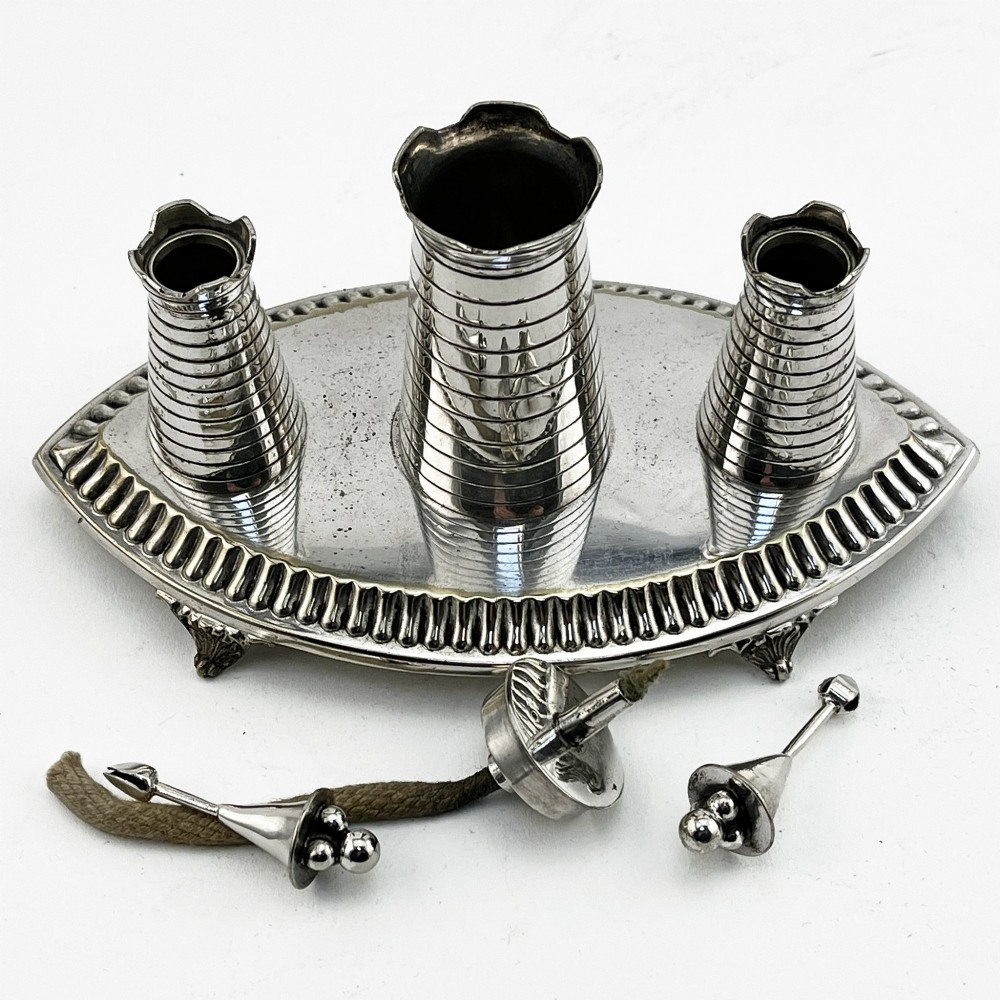 A silver-plated table cigar lighter featuring three horizontal-ribbed conical towers set on an oval tray with a gadrooned border and scrolled feet. View III