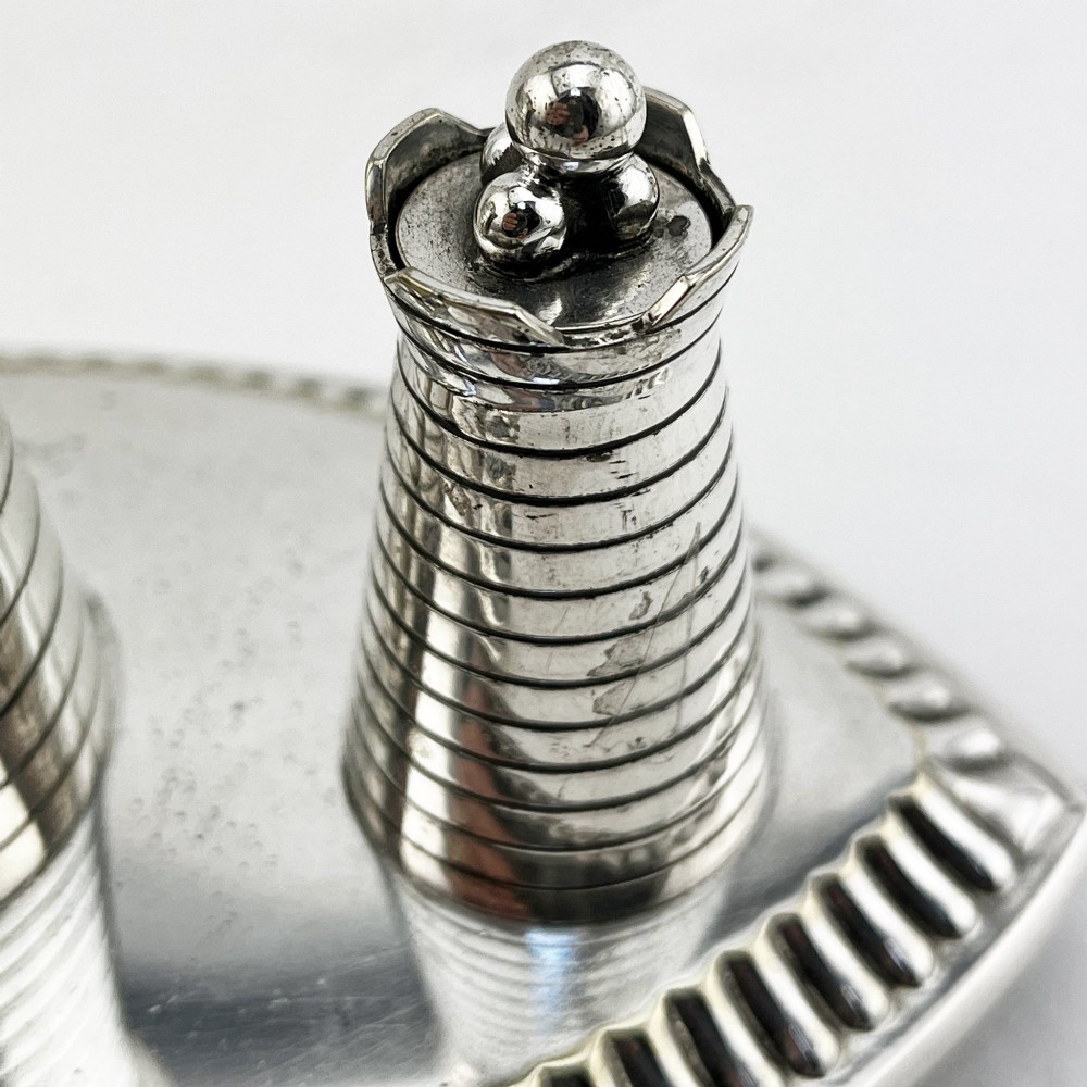 A silver-plated table cigar lighter featuring three horizontal-ribbed conical towers set on an oval tray with a gadrooned border and scrolled feet. View IV