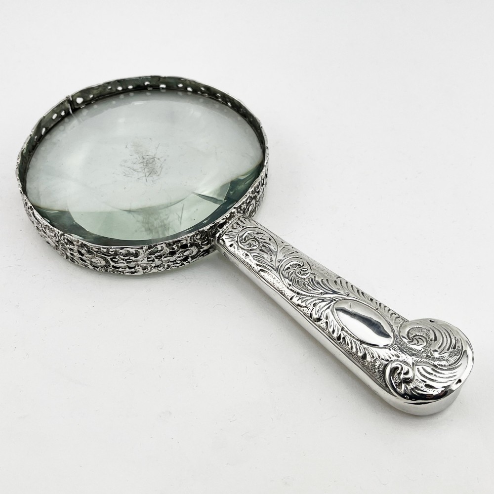An antique Victorian sterling silver magnifying glass featuring an intricately chased handle and a pierced decorative circular silver rim.