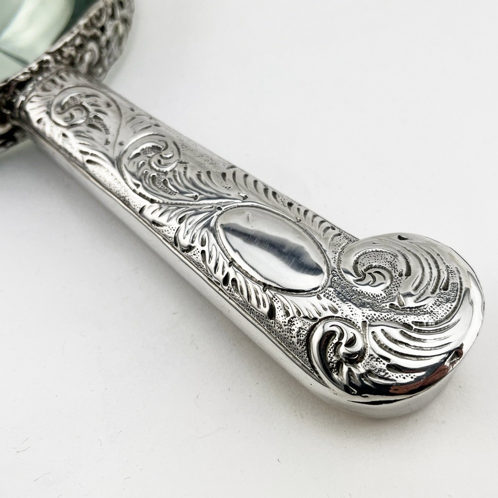 An antique Victorian sterling silver magnifying glass featuring an intricately chased handle and a pierced decorative circular silver rim. View II