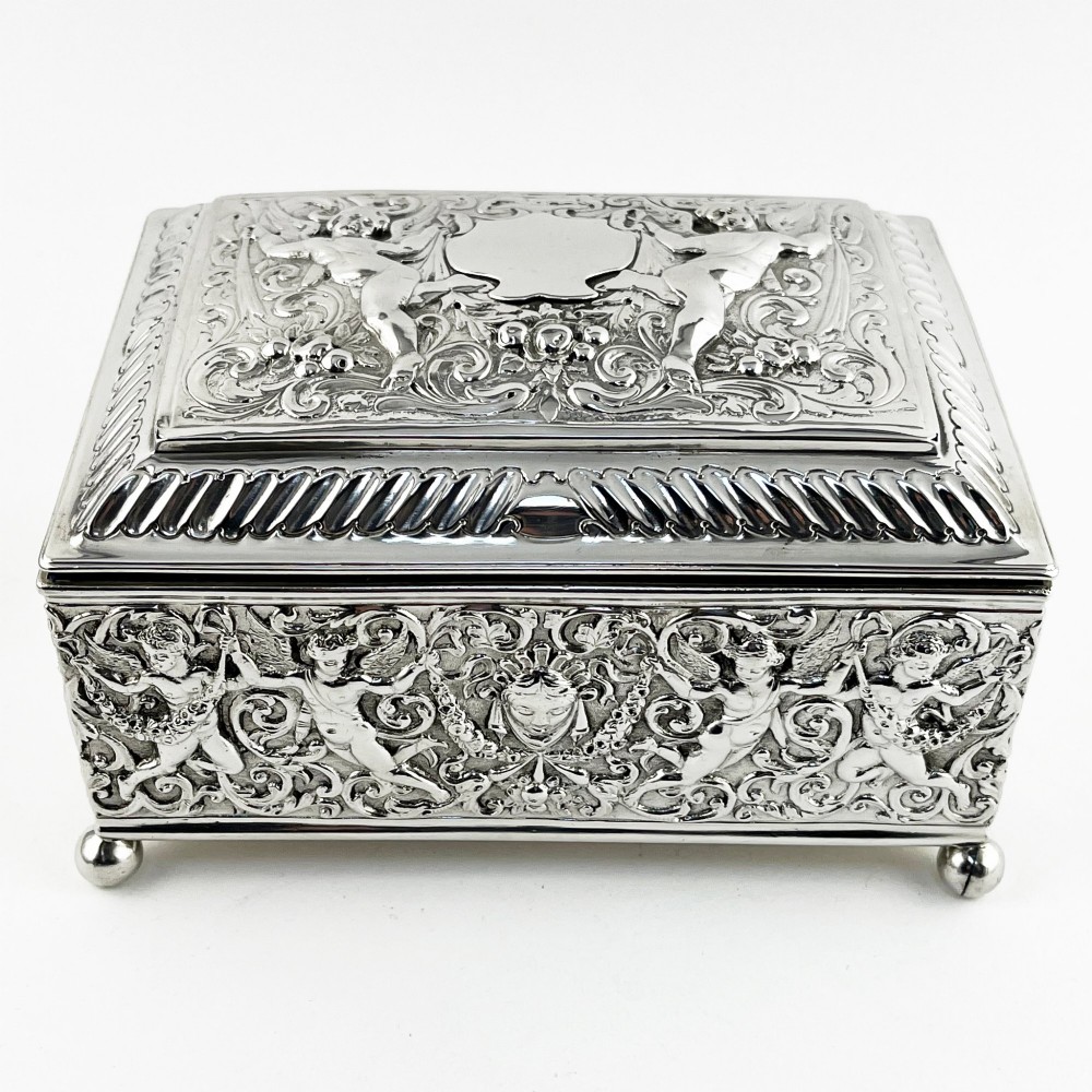 A rectangular Victorian sterling silver trinket box decorated with detailed repousse cherubs and floral scrolls, supported by four ball feet.