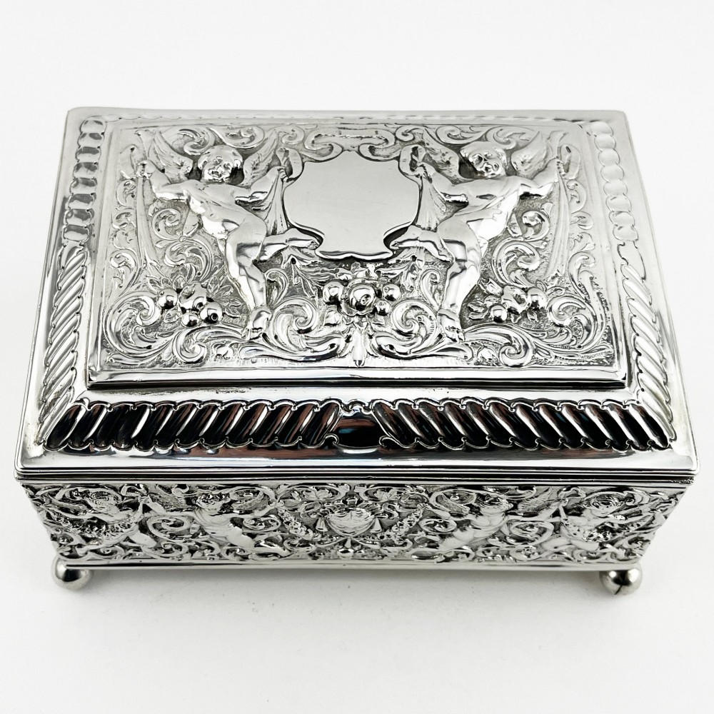 A rectangular Victorian sterling silver trinket box decorated with detailed repousse cherubs and floral scrolls, supported by four ball feet. View II