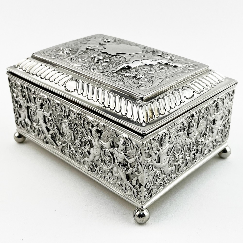 A rectangular Victorian sterling silver trinket box decorated with detailed repousse cherubs and floral scrolls, supported by four ball feet. View IV
