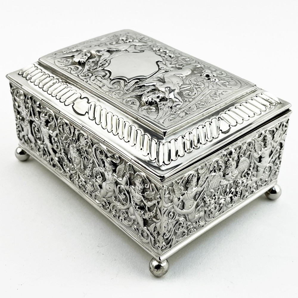 A rectangular Victorian sterling silver trinket box decorated with detailed repousse cherubs and floral scrolls, supported by four ball feet. View V