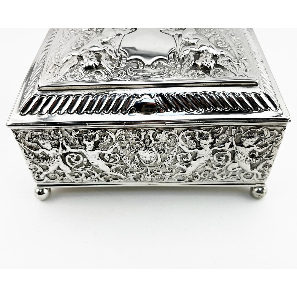 A rectangular Victorian sterling silver trinket box decorated with detailed repousse cherubs and floral scrolls, supported by four ball feet. View VI