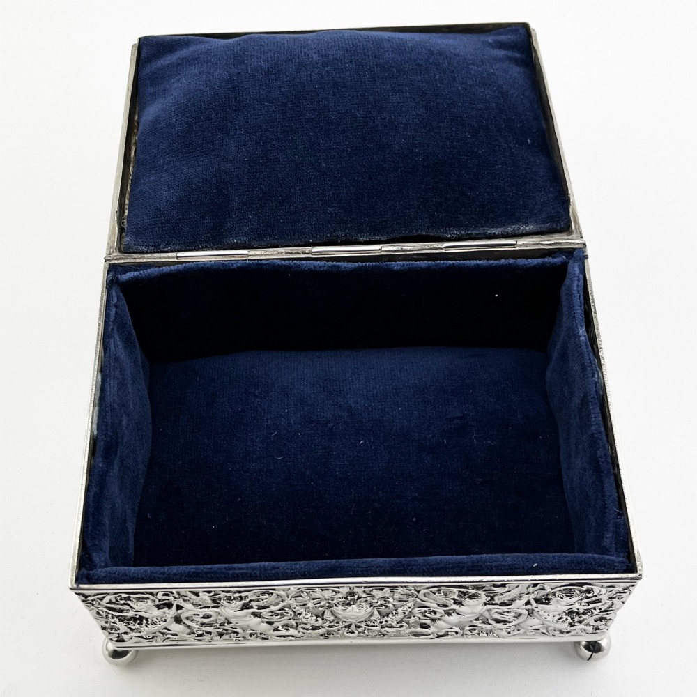 A rectangular Victorian sterling silver trinket box decorated with detailed repousse cherubs and floral scrolls, supported by four ball feet. View VII