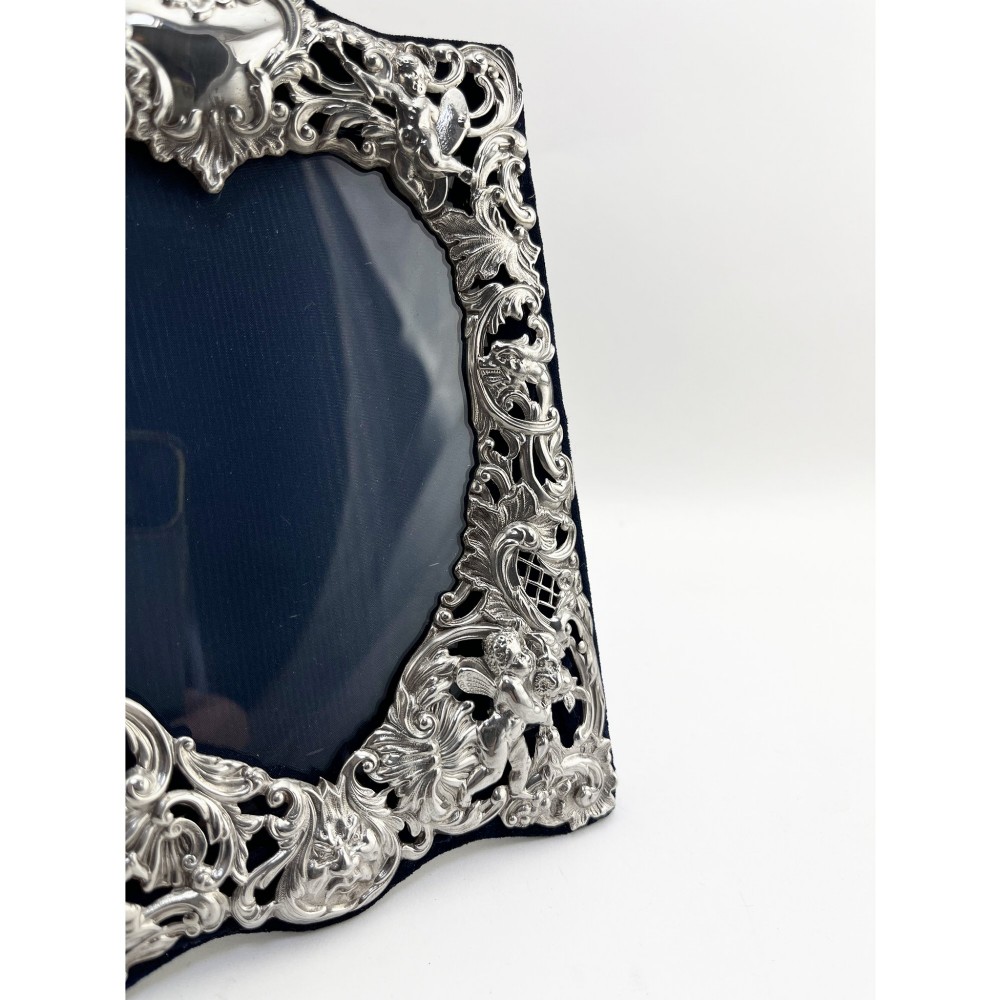 An ornate Victorian sterling silver double photo frame featuring elaborate pierced scrollwork, cherubs, and two heart-shaped apertures backed with dark velvet. View III
