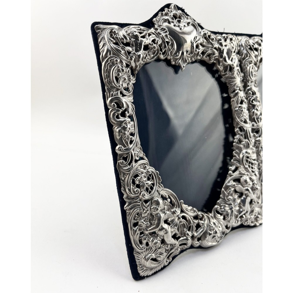 An ornate Victorian sterling silver double photo frame featuring elaborate pierced scrollwork, cherubs, and two heart-shaped apertures backed with dark velvet. View IV