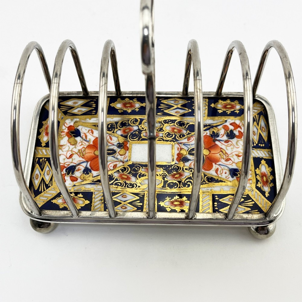 A late Victorian silver-plated six-slot toast rack featuring an arched wire frame, carrying handle, ball feet, and an Imari pattern porcelain base in cobalt blue, red, and gold. View II
