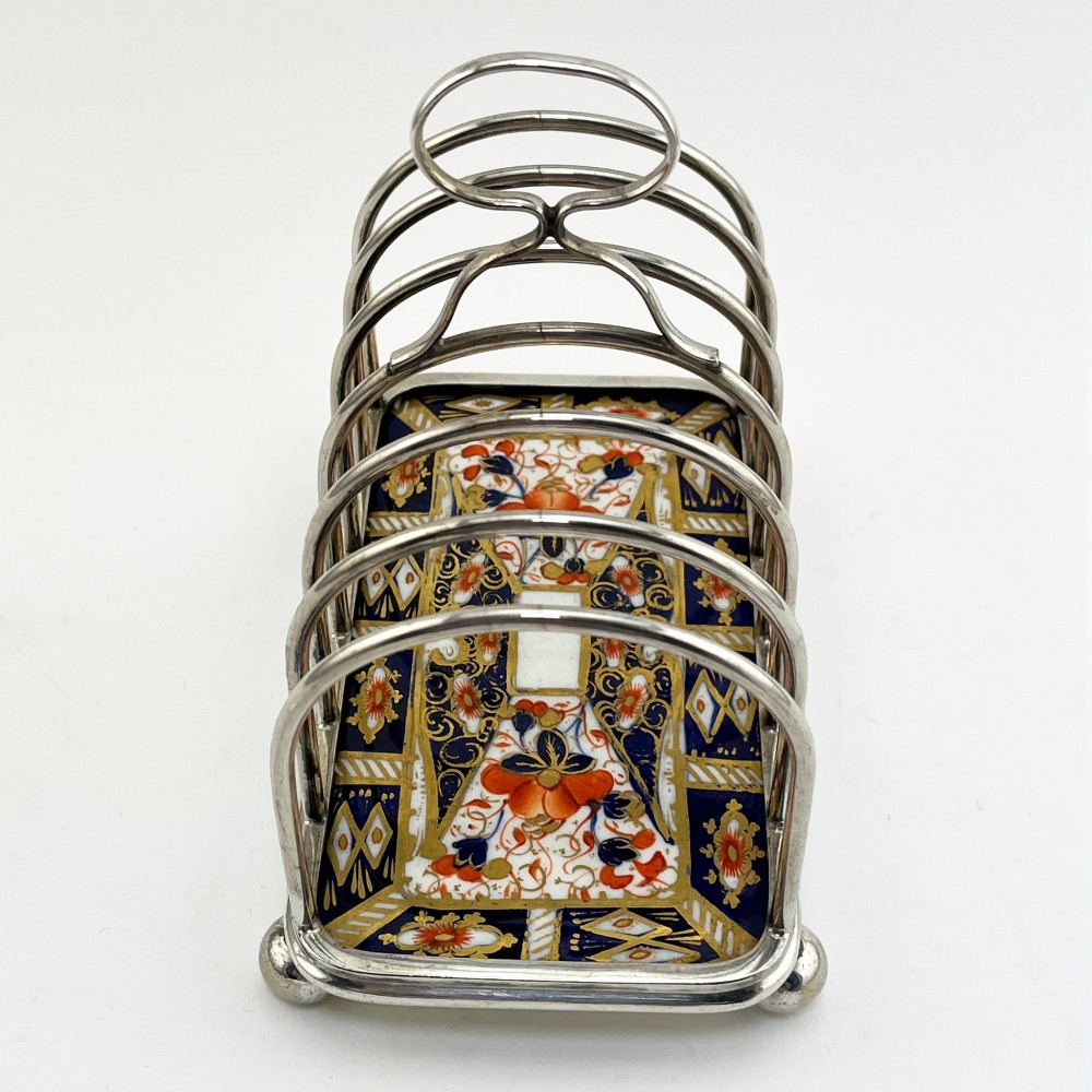 A late Victorian silver-plated six-slot toast rack featuring an arched wire frame, carrying handle, ball feet, and an Imari pattern porcelain base in cobalt blue, red, and gold. View III