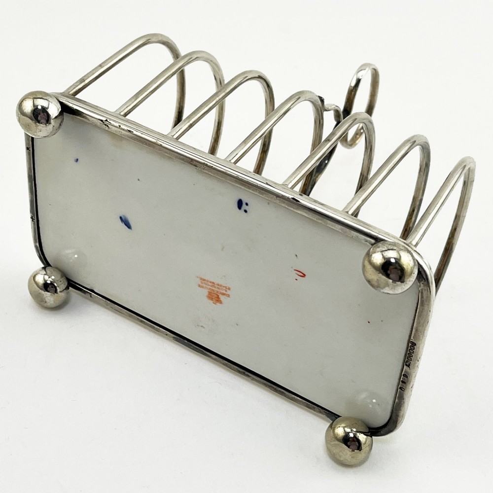 A late Victorian silver-plated six-slot toast rack featuring an arched wire frame, carrying handle, ball feet, and an Imari pattern porcelain base in cobalt blue, red, and gold. View IV