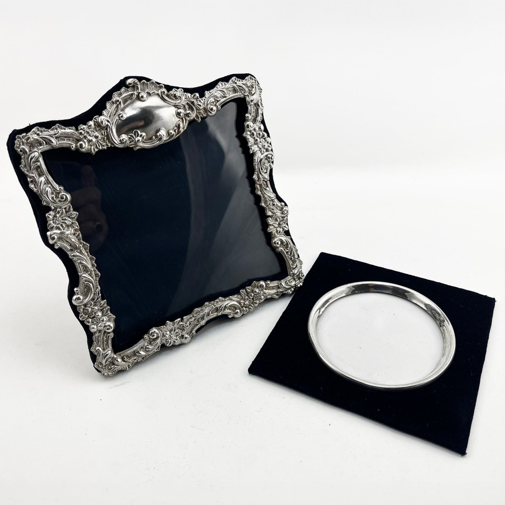 An ornate Edwardian sterling silver picture frame featuring chased floral scrollwork, a blank top cartouche, and a dark velvet mount with a central circular aperture. View II