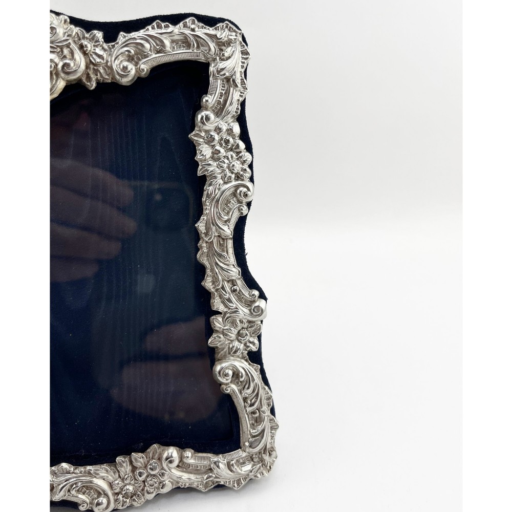 An ornate Edwardian sterling silver picture frame featuring chased floral scrollwork, a blank top cartouche, and a dark velvet mount with a central circular aperture. View III