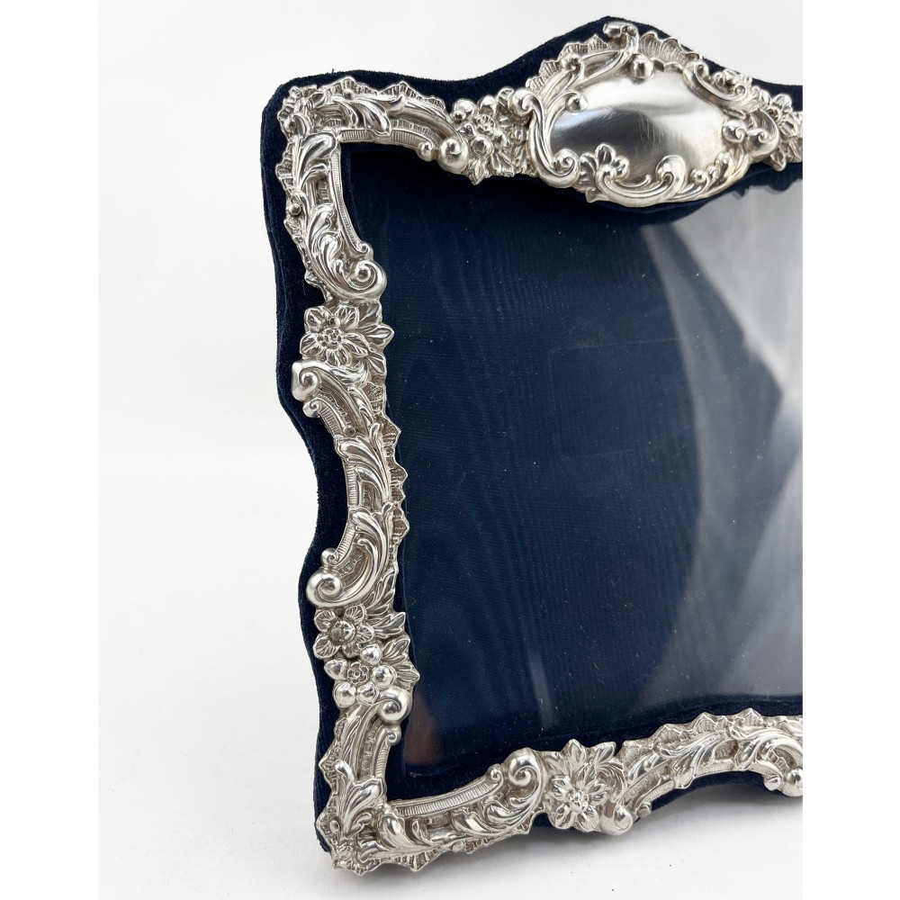 An ornate Edwardian sterling silver picture frame featuring chased floral scrollwork, a blank top cartouche, and a dark velvet mount with a central circular aperture. View IV