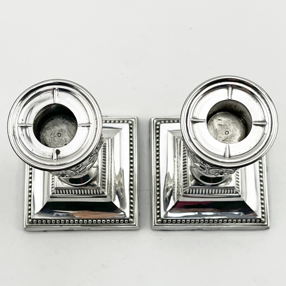 A pair of hallmarked Edwardian sterling silver candlesticks featuring urn-shaped stems with swag motifs and stepped beaded square bases. View II