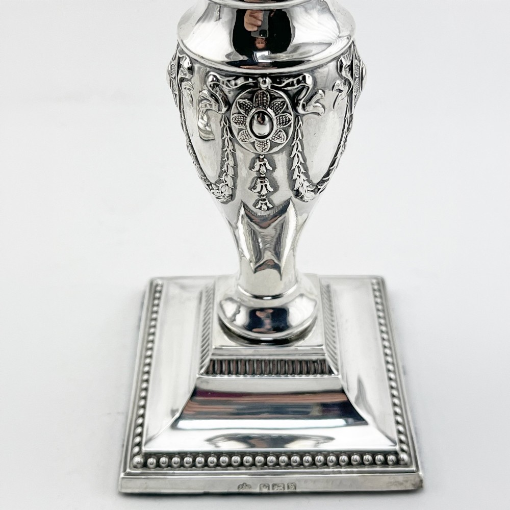 A pair of hallmarked Edwardian sterling silver candlesticks featuring urn-shaped stems with swag motifs and stepped beaded square bases. View III