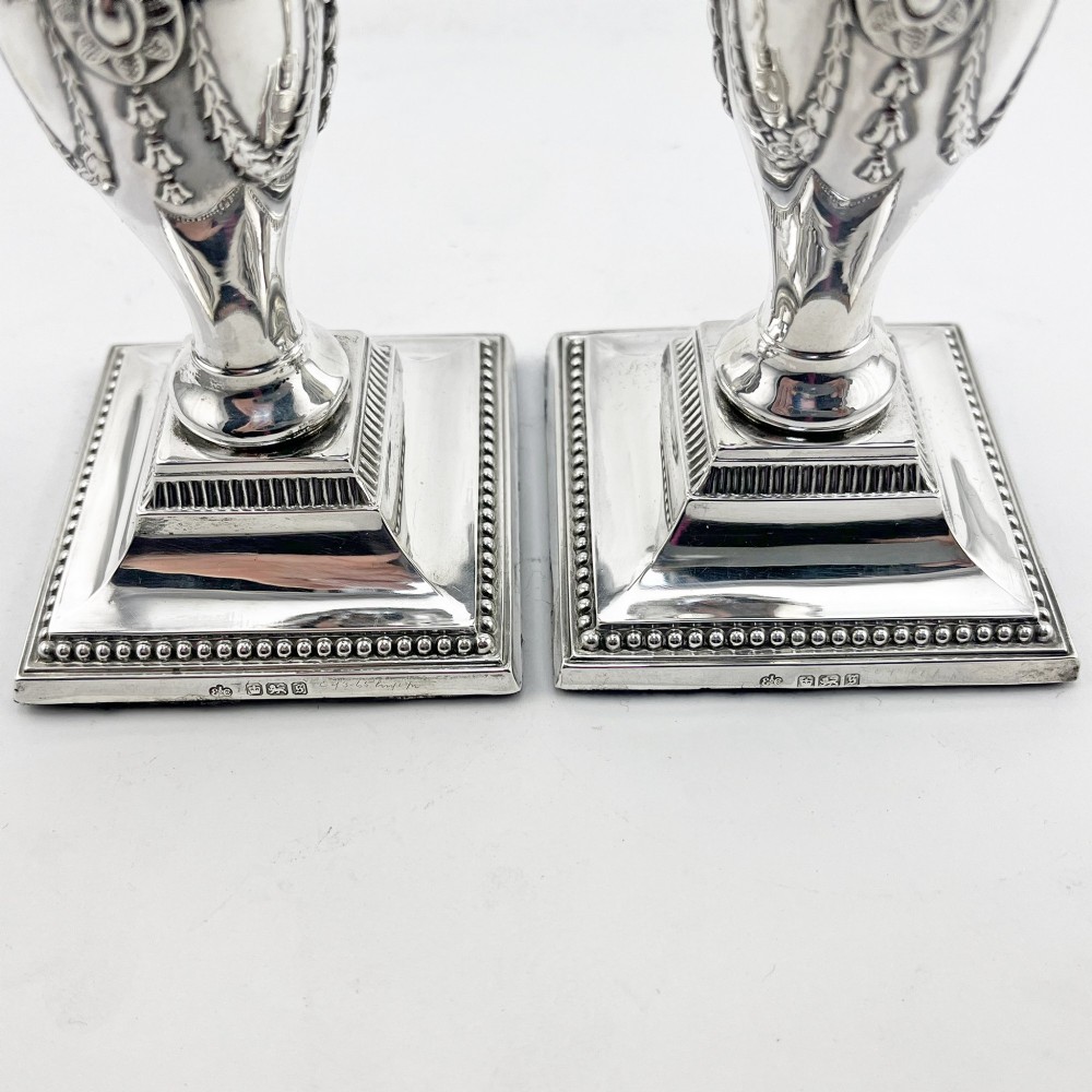 A pair of hallmarked Edwardian sterling silver candlesticks featuring urn-shaped stems with swag motifs and stepped beaded square bases. View IV