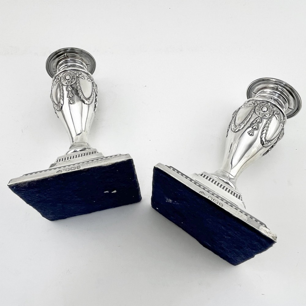 A pair of hallmarked Edwardian sterling silver candlesticks featuring urn-shaped stems with swag motifs and stepped beaded square bases. View VII