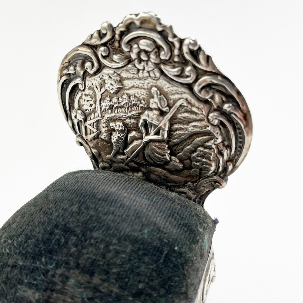 A miniature sterling silver pin cushion crafted in the shape of an ornate chair with an embossed backrest and dark velvet seat pad. View II