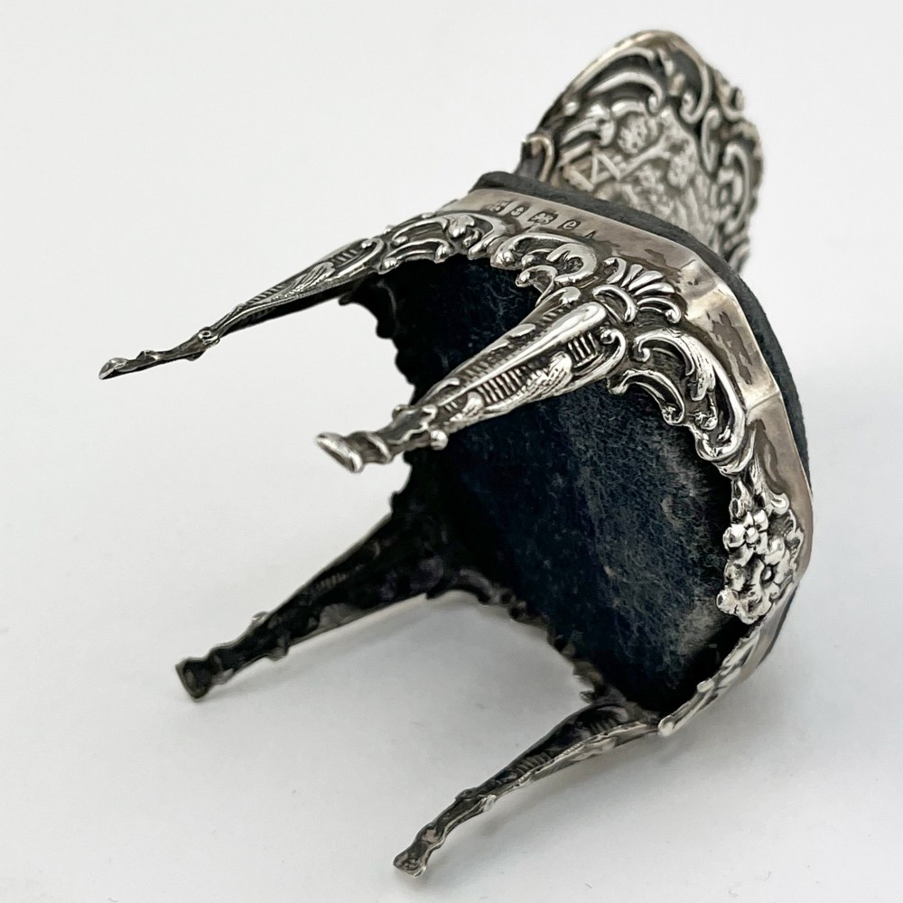 A miniature sterling silver pin cushion crafted in the shape of an ornate chair with an embossed backrest and dark velvet seat pad. View VI