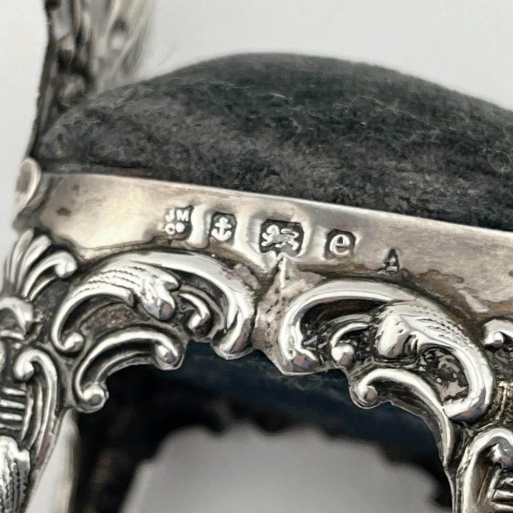 A miniature sterling silver pin cushion crafted in the shape of an ornate chair with an embossed backrest and dark velvet seat pad. View VII