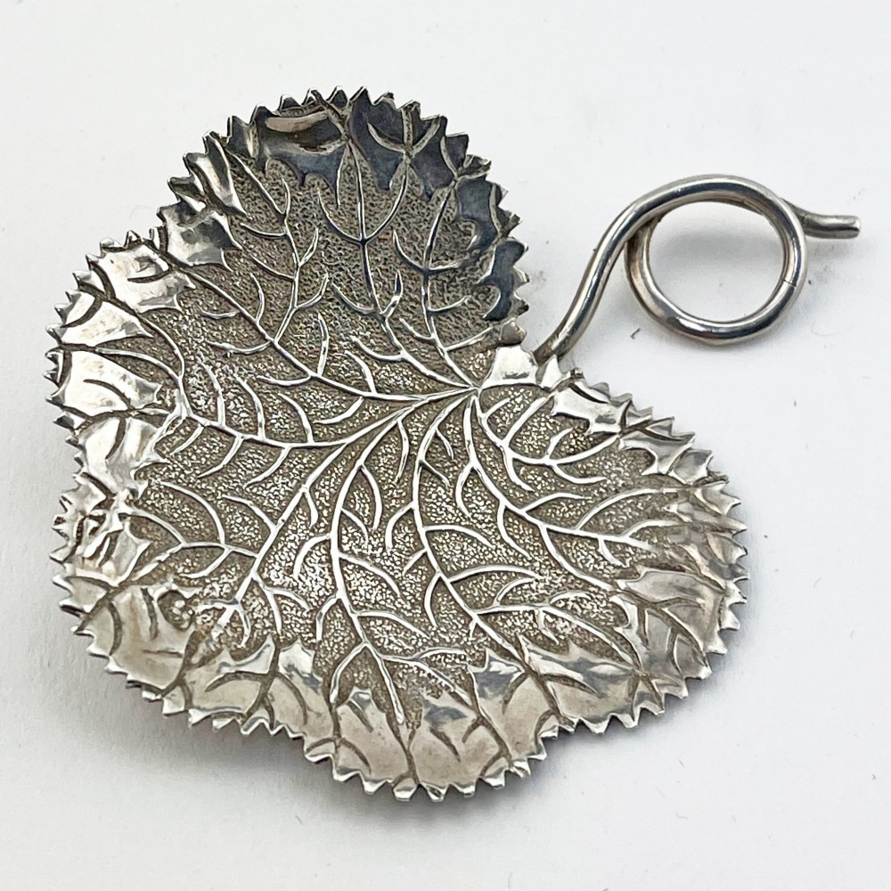 A Georgian sterling silver tea caddy spoon fashioned in the shape of a serrated leaf with engraved vein detailing and a coiled ring handle.