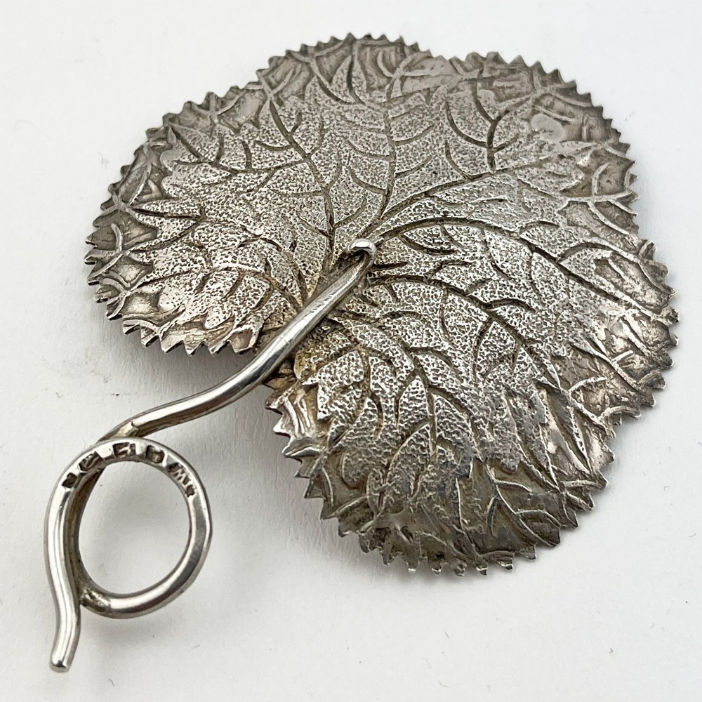 A Georgian sterling silver tea caddy spoon fashioned in the shape of a serrated leaf with engraved vein detailing and a coiled ring handle. View II