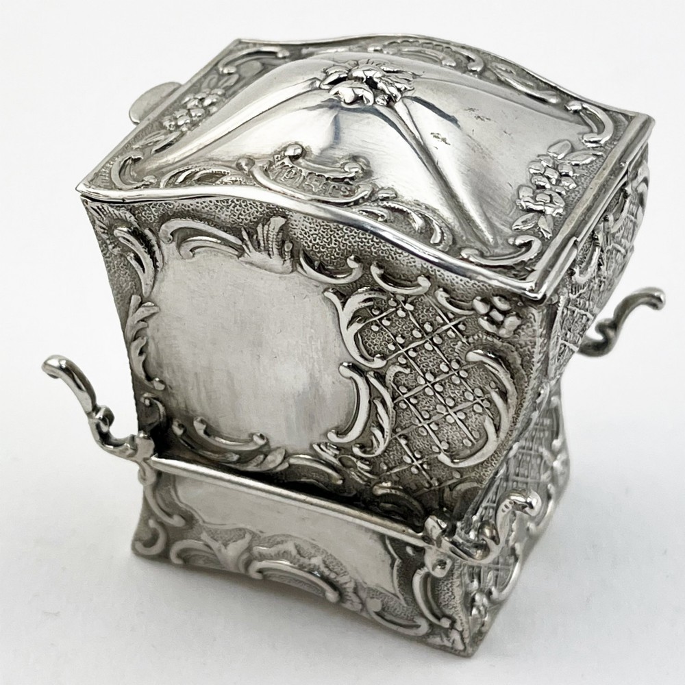 A Victorian sterling silver playing card case designed in the form of a sedan chair with embossed floral and scroll motifs.