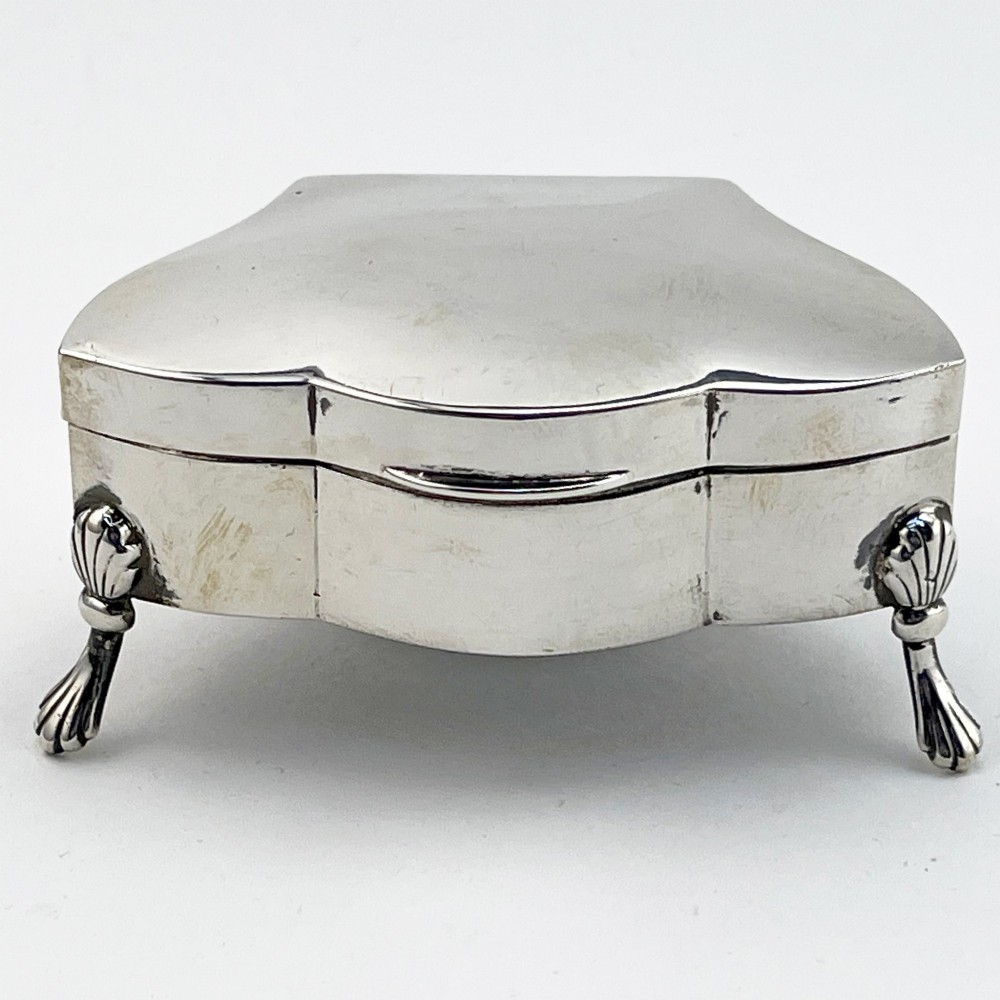 A polished sterling silver trinket box featuring a contoured lid and four shell-motif feet.
