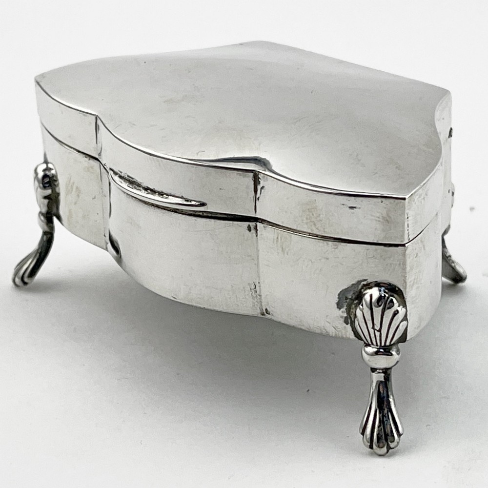 A polished sterling silver trinket box featuring a contoured lid and four shell-motif feet. View II